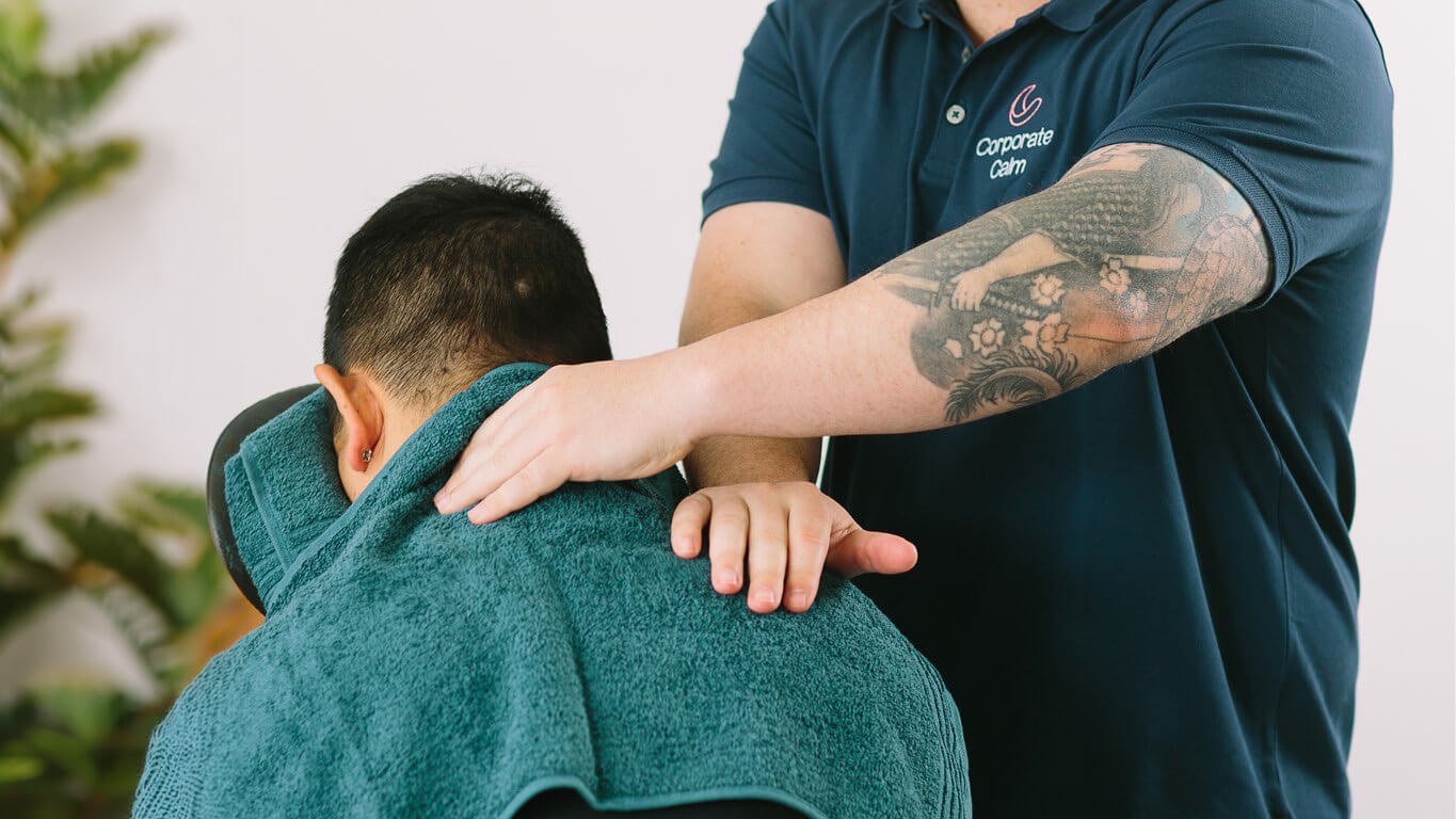 Massage therapist delivering an on-site chair massage session to an employee in his office