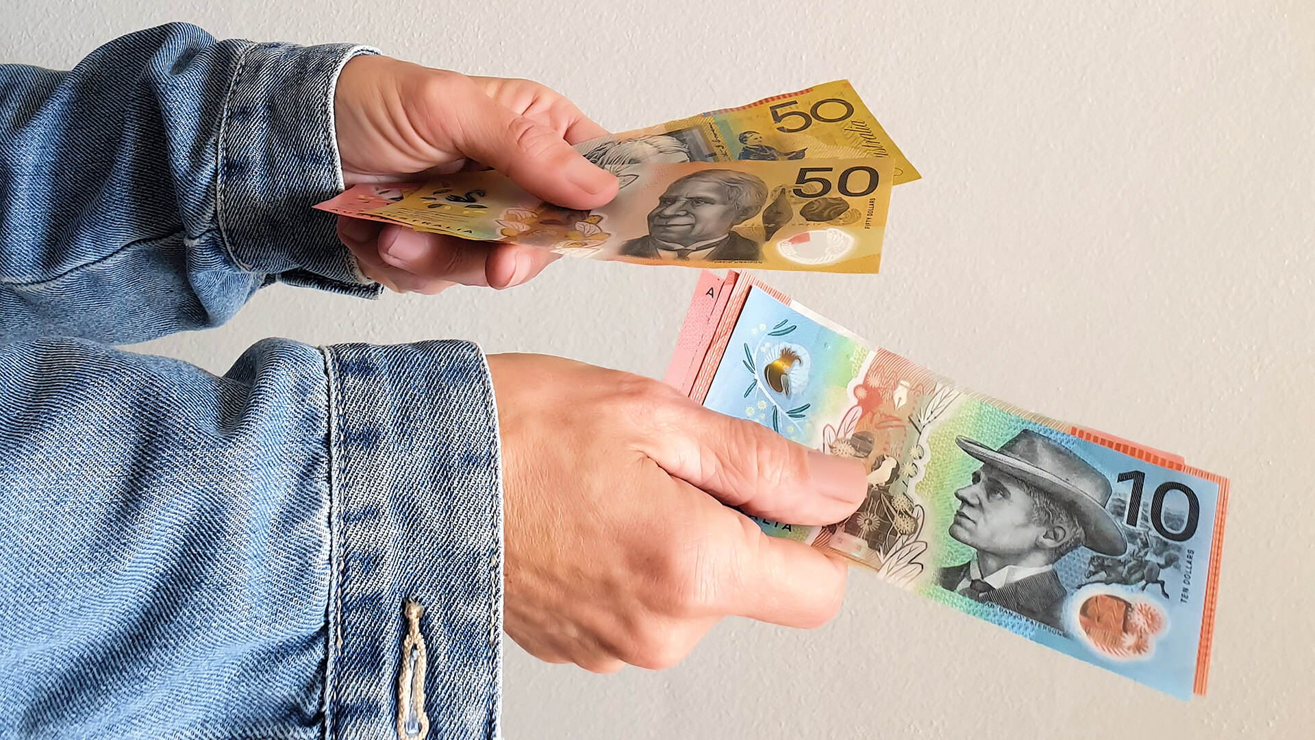 Two hands exchanging Australian fifty and ten dollar notes representing the cost of workplace presenteeism