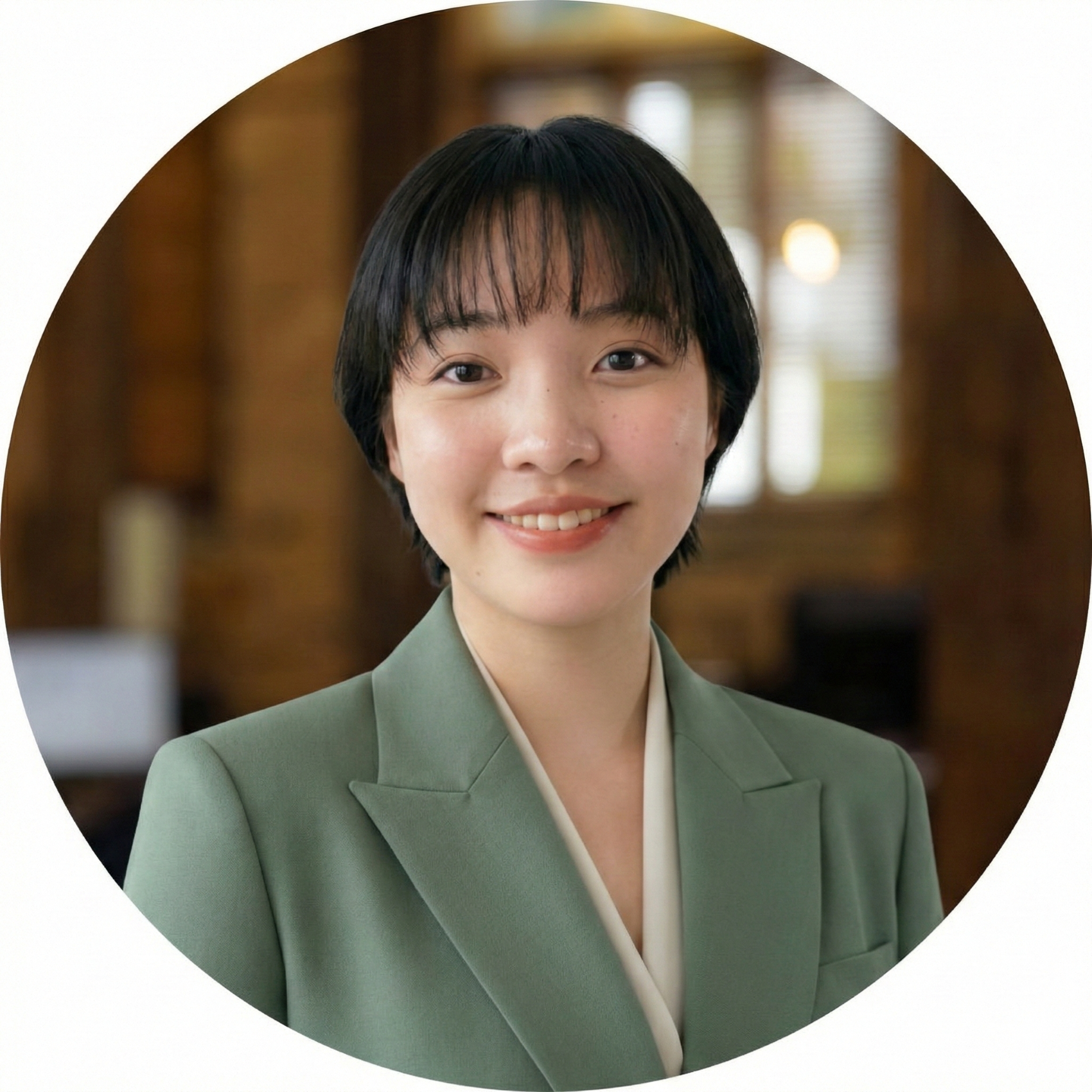 Smiling young woman with short black hair wearing a green blazer in an indoor setting.