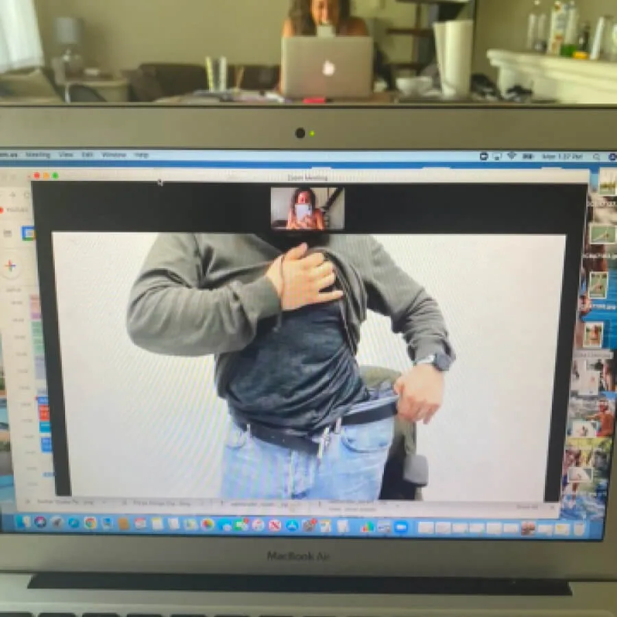 Video call on a laptop screen shows a person lifting their shirt to reveal their stomach and pulling out loose jeans waistband.