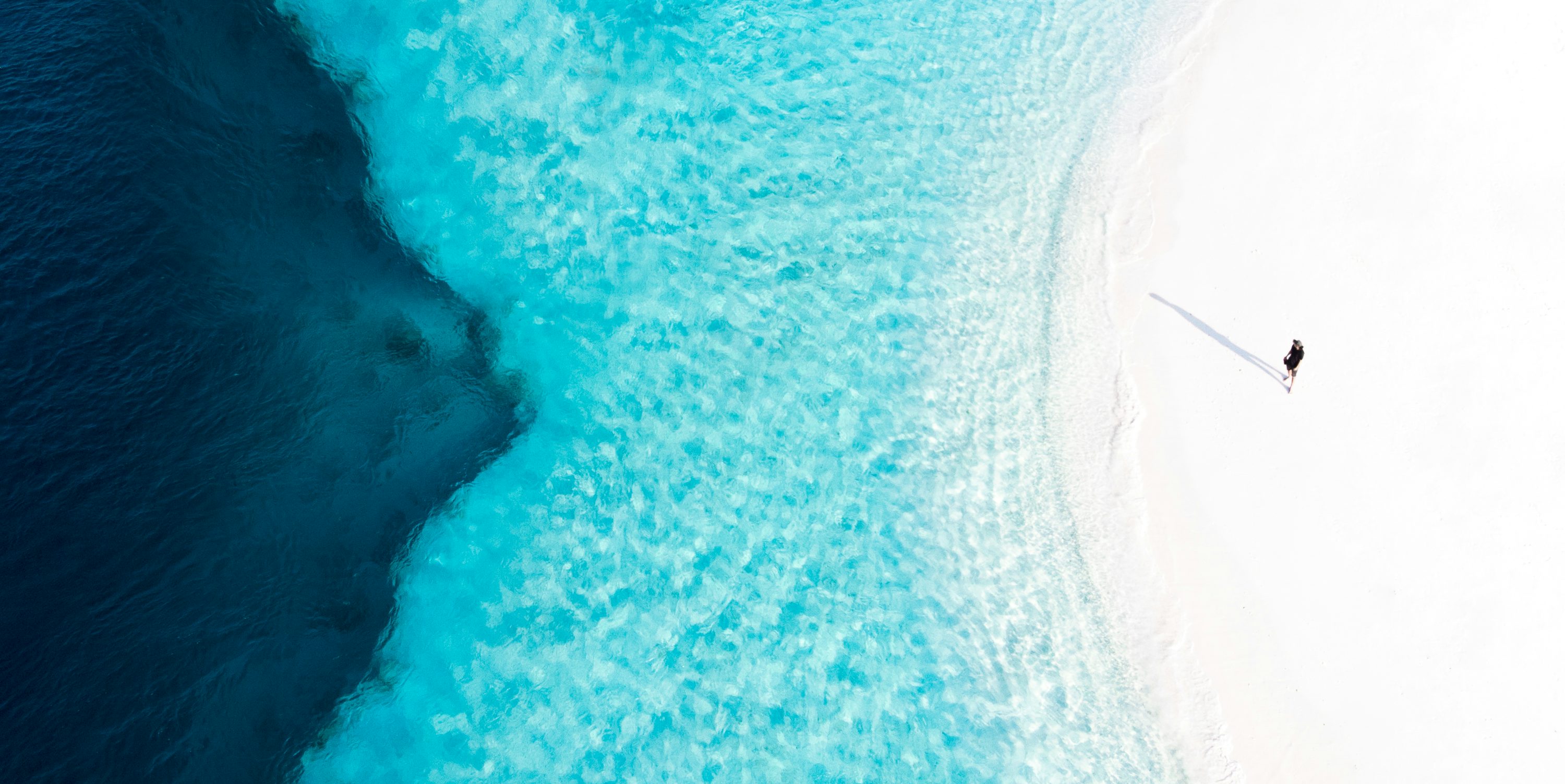 Aerial view of clear turquoise ocean water and white sand beach, representing a tropical destination.