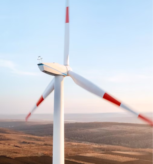 Wind turbine with red markings on blades spinning over dry, hilly landscape under a clear sky.
