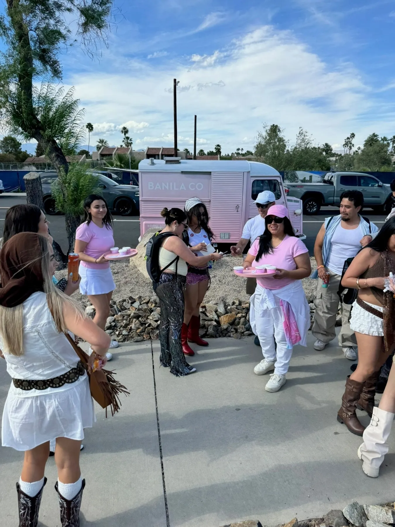 Banila Co ambassadors distributing samples to festivalgoers near a Coachella shuttle stop with a Retro Roll activation van nearby. 