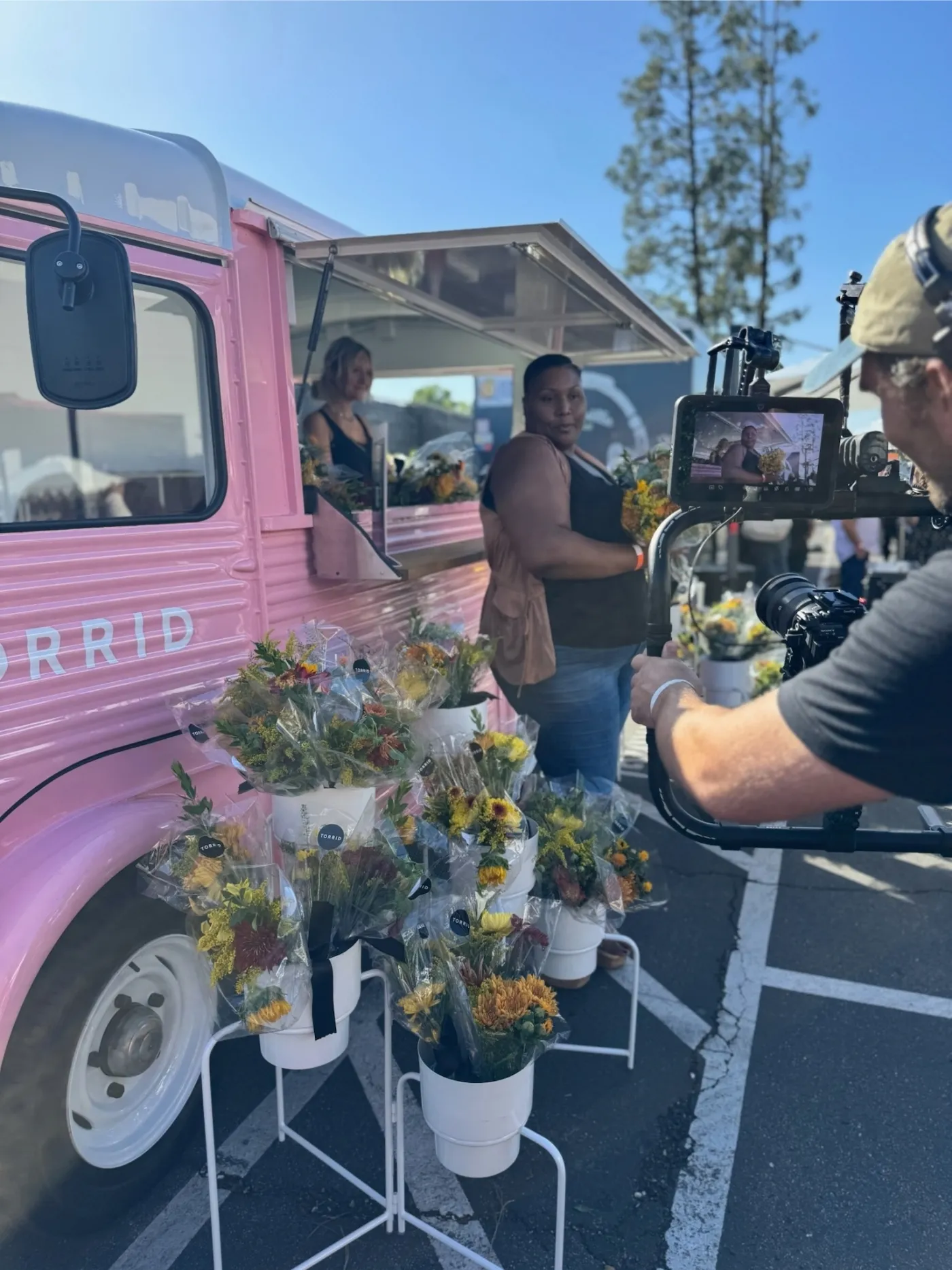 Professional camera crew filming a participant beside the Torrid-branded Citroën flower truck