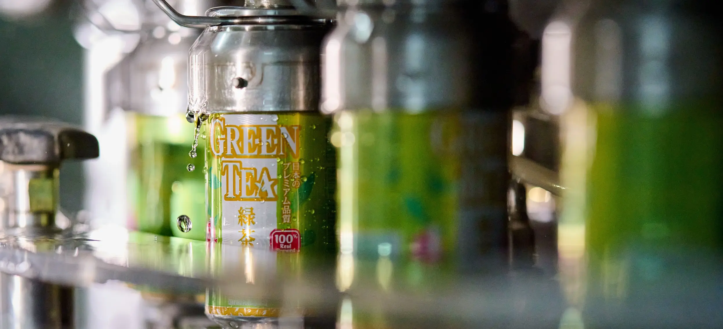 Close-up of green tea cans with water droplets, part of a bottling or filling machine.