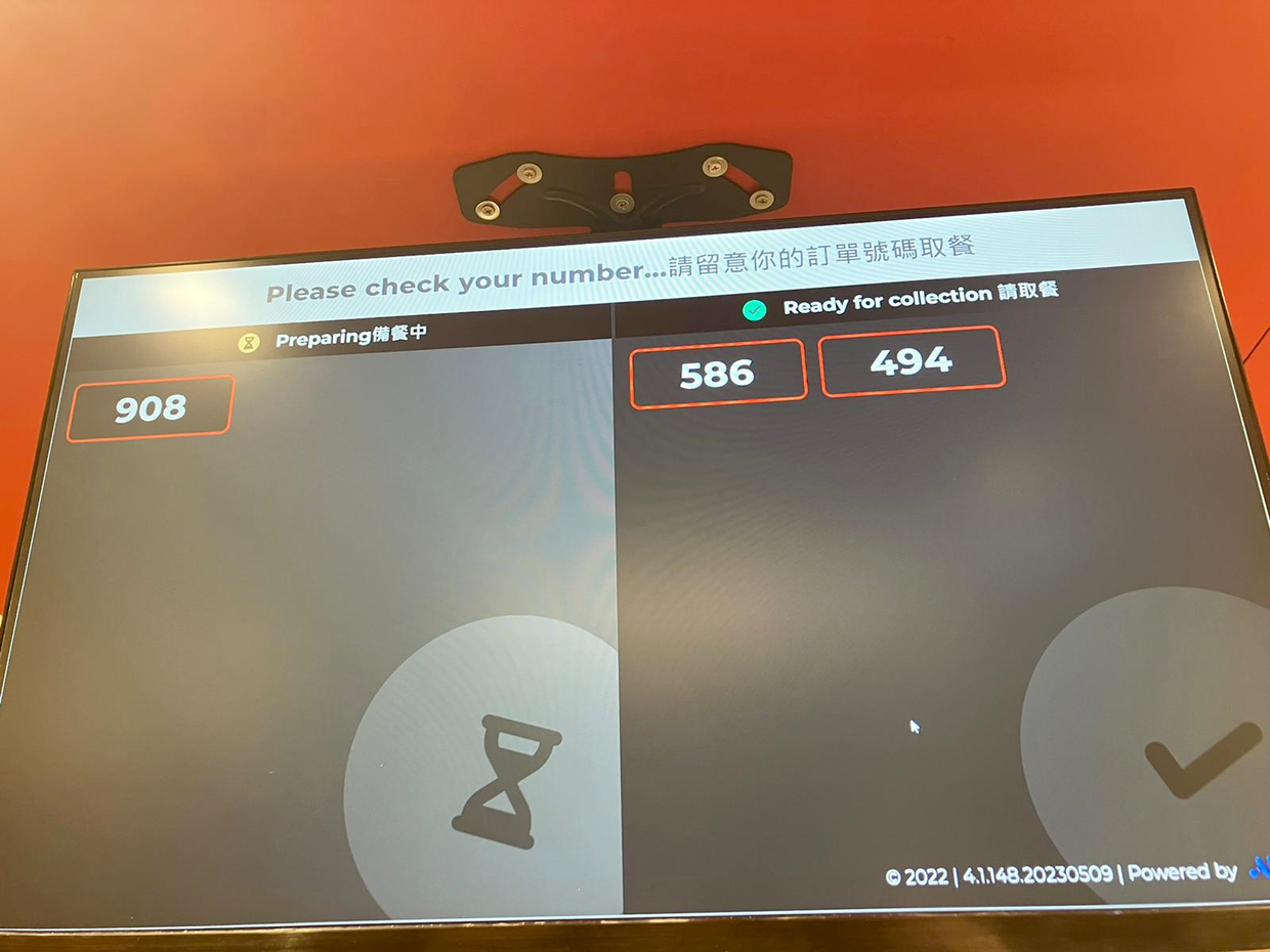 Digital order pickup screen showing order number 908 as preparing with hourglass icon, and numbers 586 and 494 ready for collection with checkmark icon.