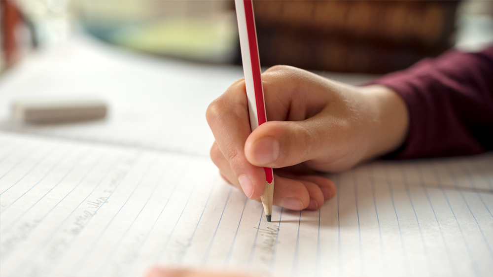 Bild på barnhand som skriver i anteckningsblock.