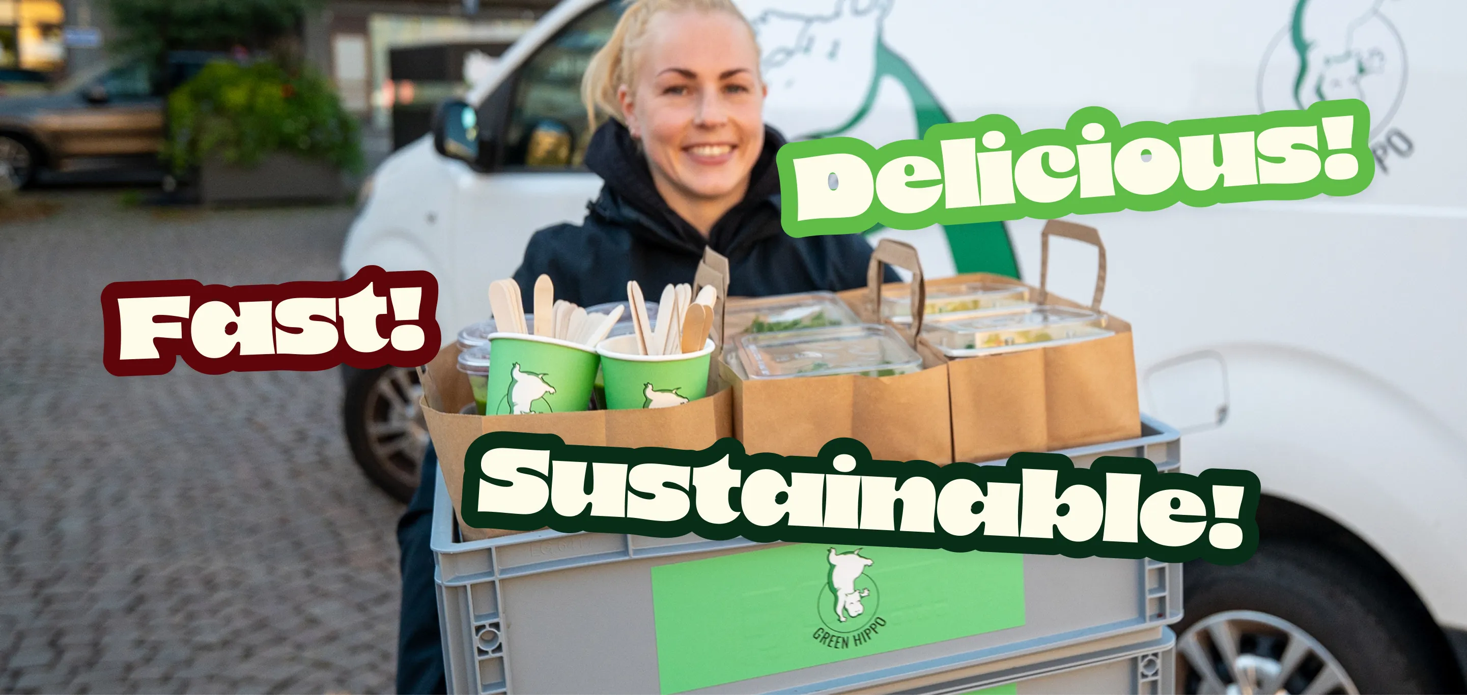Hymyilevä nainen kantaa laatikkoa, jossa on ekologisia ruoka-annoksia ja kertakäyttövälineitä Green Hippo -logolla.