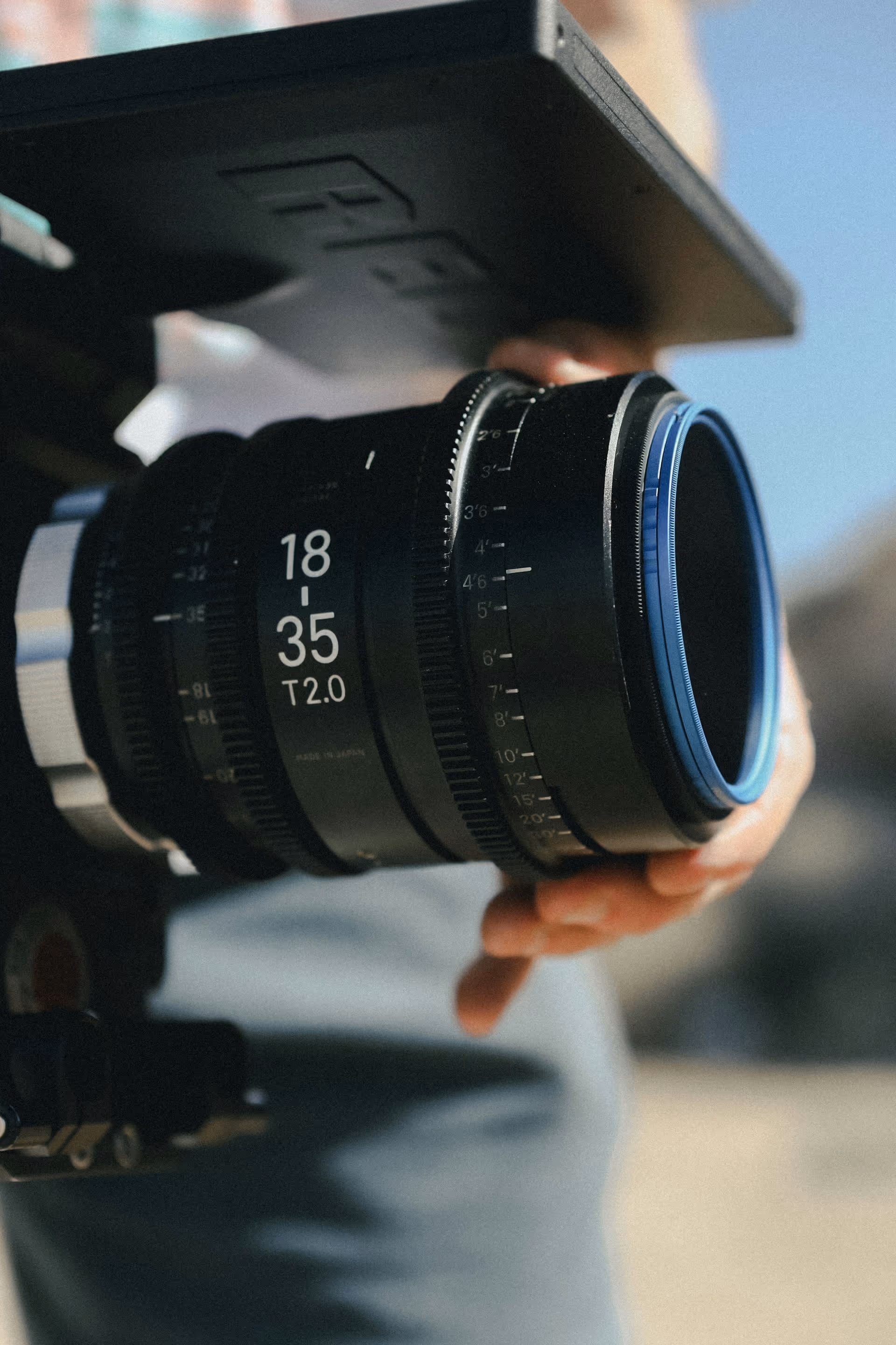 Close-up of a person adjusting a camera lens marked 18-35 T2.0 on a video camera rig.