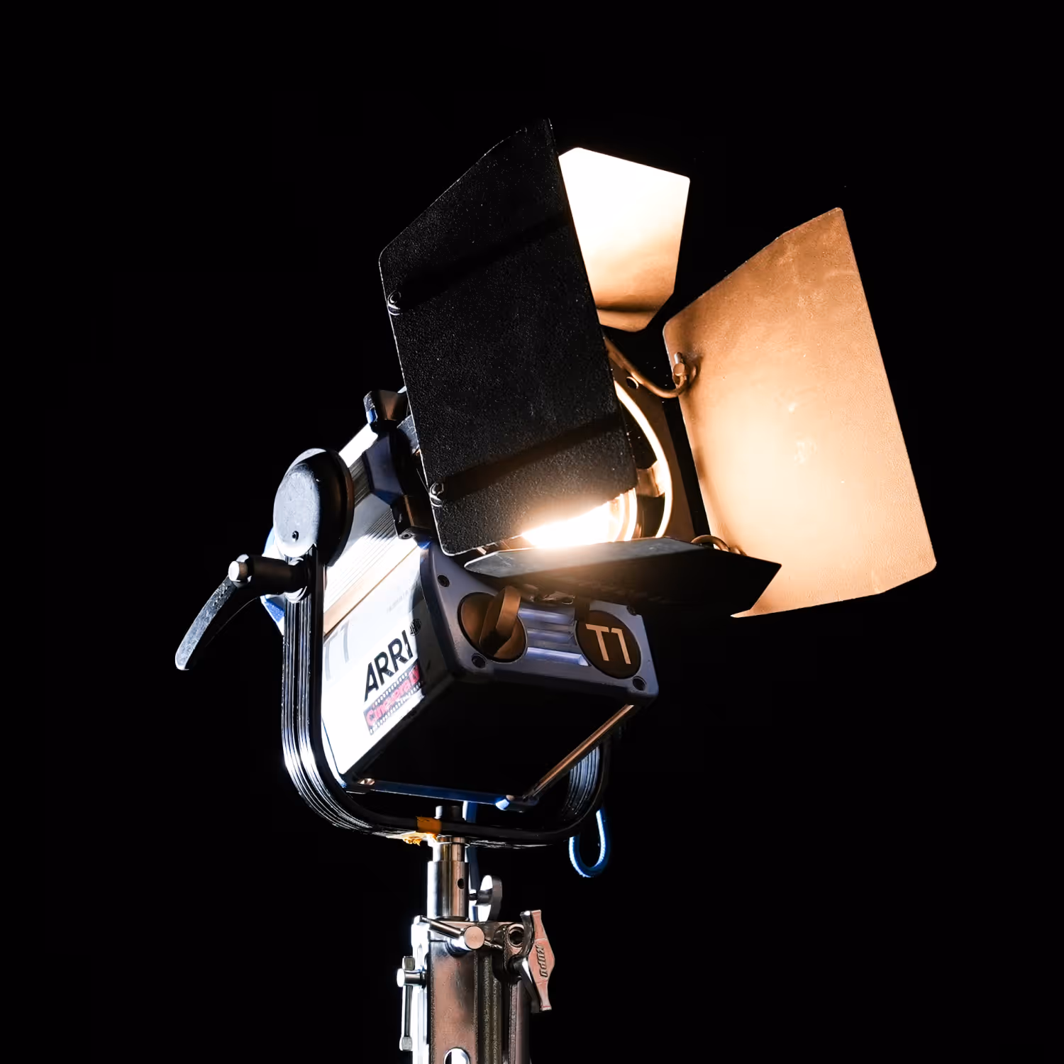 ARRI T1 professional studio light with barn doors on a metal stand against black background.