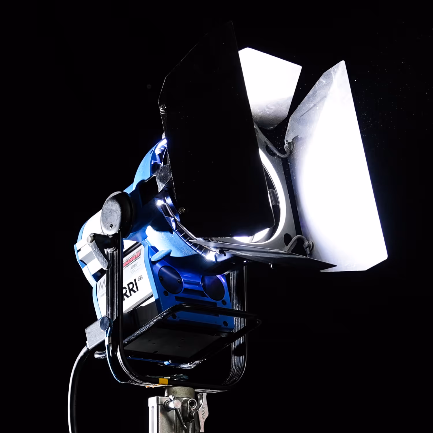 Close-up of a blue ARRI studio light with barn doors, turned on against a black background.