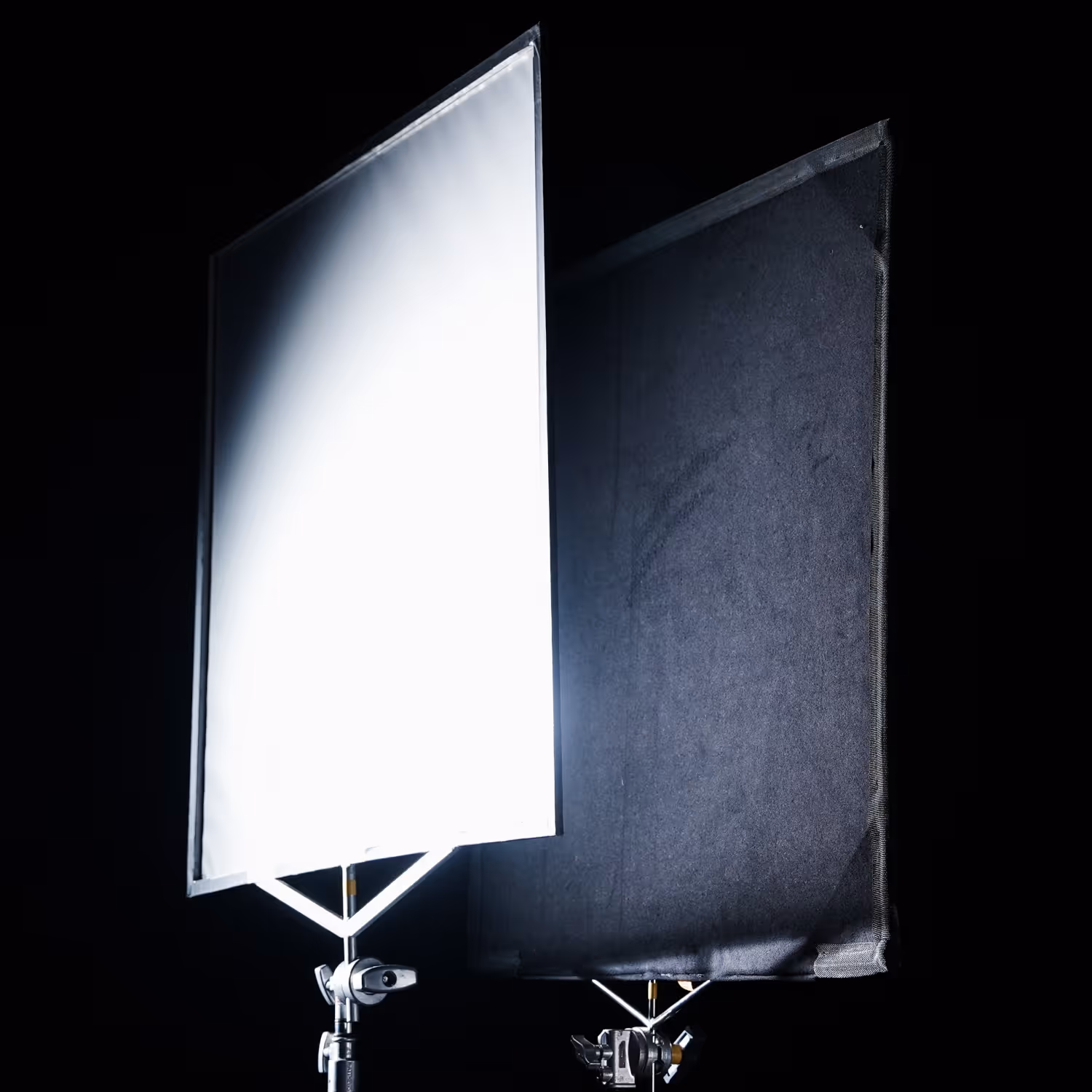 Two studio light diffusers on stands, one glowing white and the other black in a dark background.