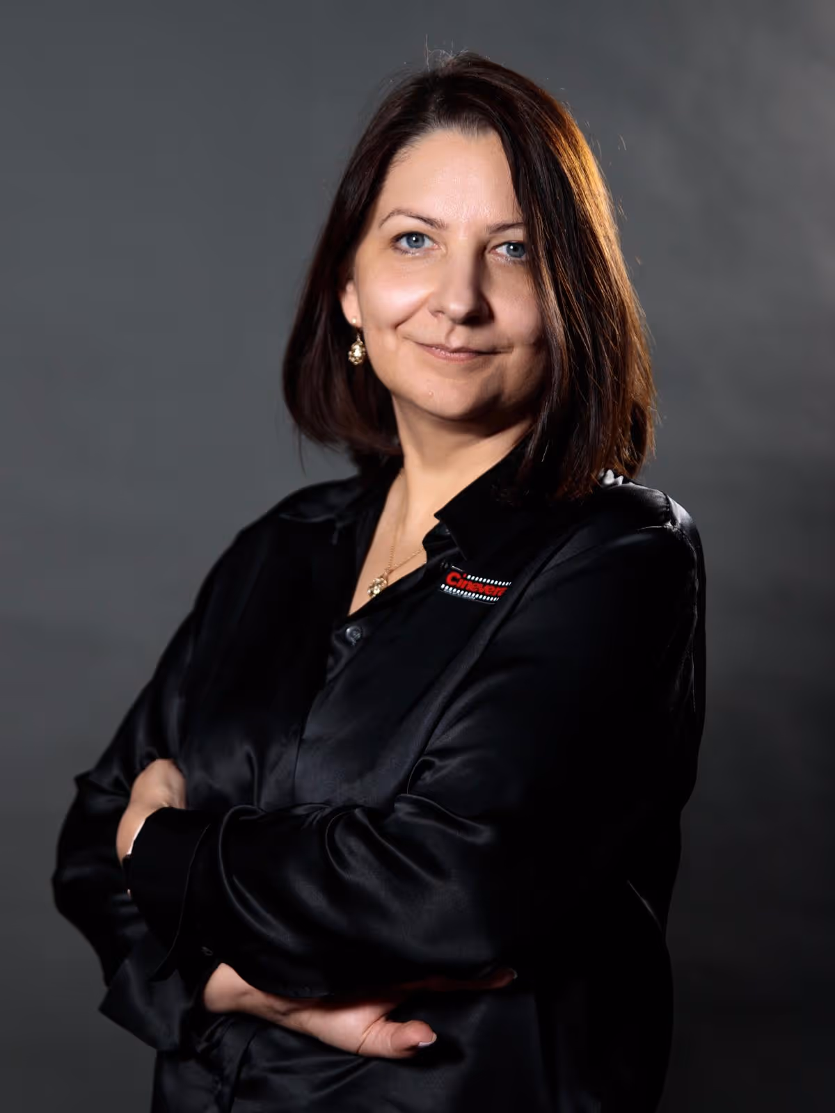 Woman with shoulder-length brown hair wearing a black shirt with arms crossed, smiling slightly.