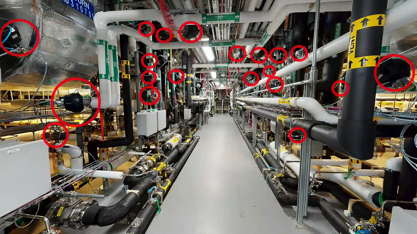 A gray space corridor at AstraZeneca's Frederick site with pipework overhead and about twenty valves circled in red
