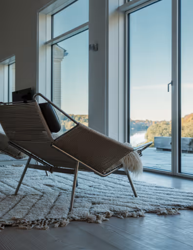 Modern lounge chair with a black pillow on a textured rug next to large glass sliding doors showing a scenic outdoor view.