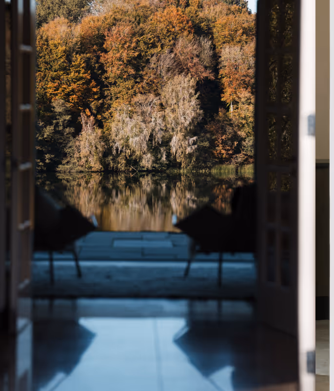 View through an open doorway showing chairs facing a lake with autumn trees reflected in the water.