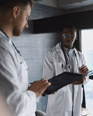 Two doctors in white lab coats discussing medical information, one holding a tablet.