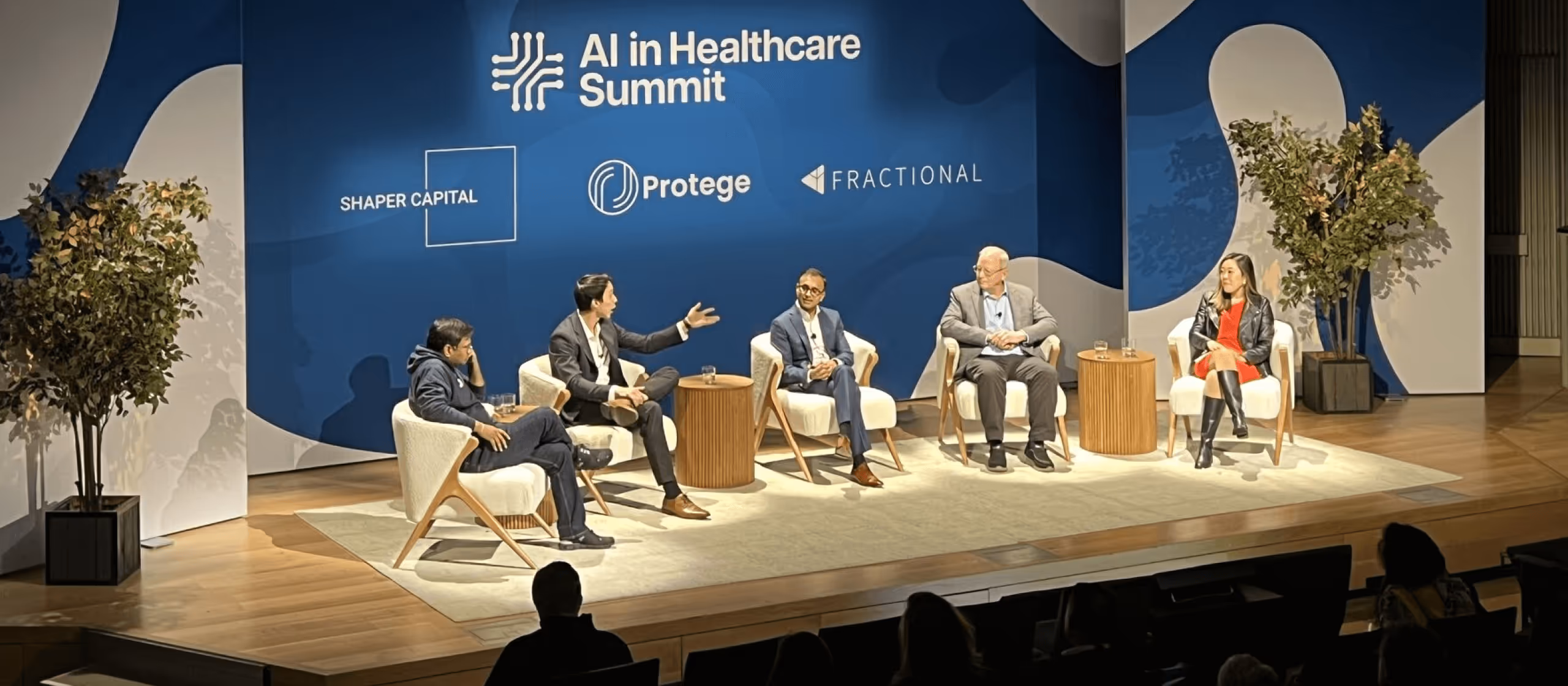 Panel of five speakers seated on stage at AI in Healthcare Summit with blue backdrop and sponsor logos.