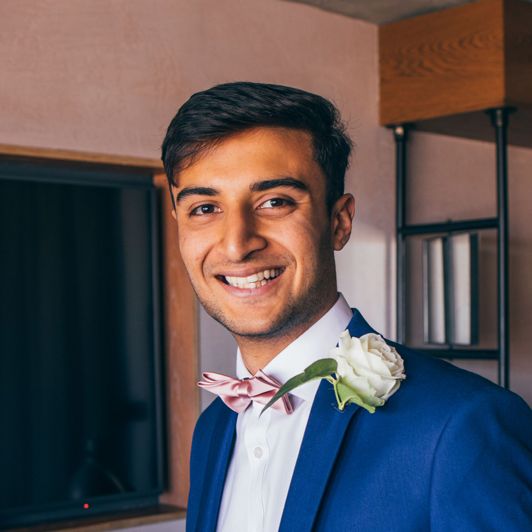 Smiling man wearing a blue suit, white shirt, pink bow tie, and white rose.