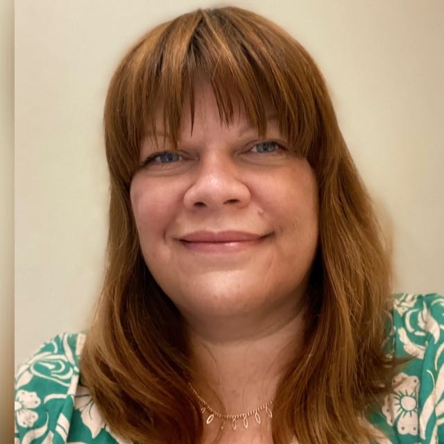 Portrait of a woman with light brown hair and bangs, smiling gently, wearing a patterned top.