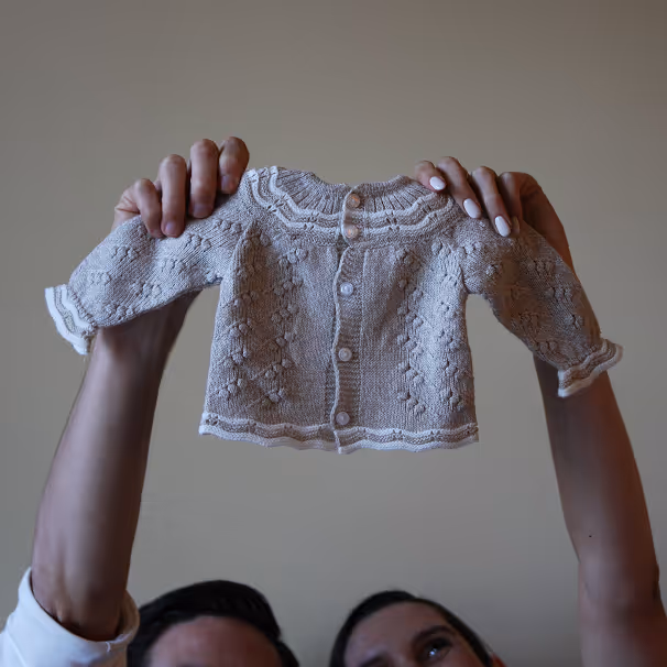 Twee handen houden een gebreide babytrui vast boven de hoofden van twee mensen.