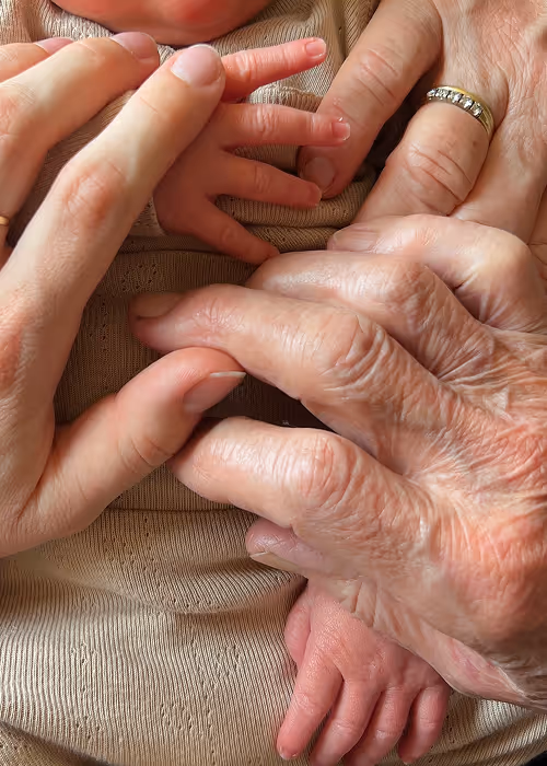 Drie generaties handen in elkaar, met een baby, een volwassen en een oudere hand met een ring.