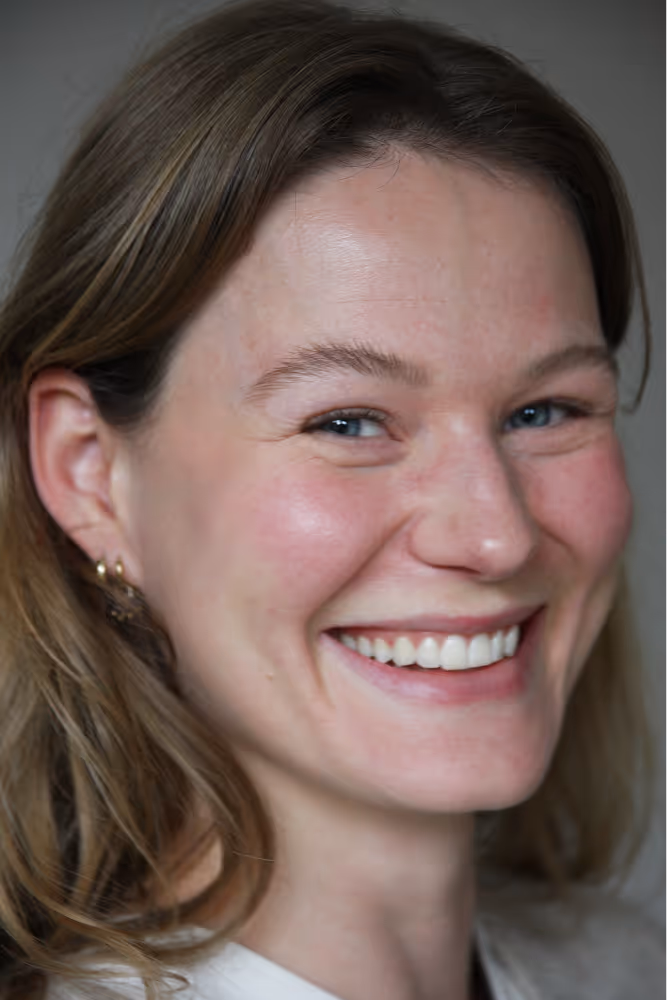 Close-up van een lachende vrouw met licht bruine haren en blauwe ogen.