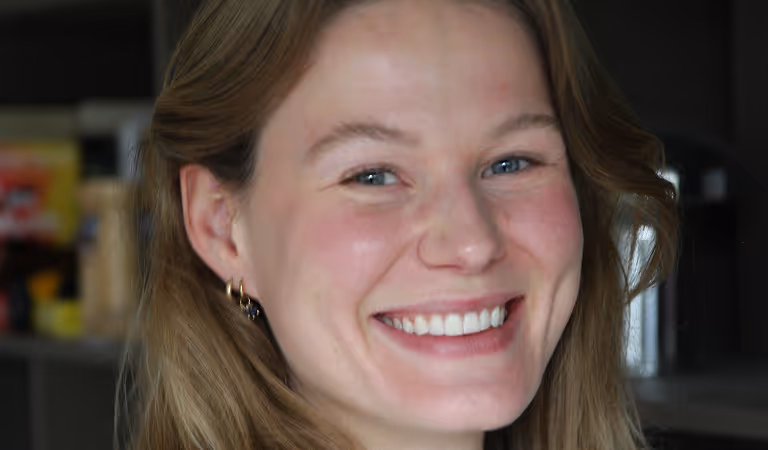 Lachende vrouw met blond haar, blauwe ogen en gouden oorbellen.