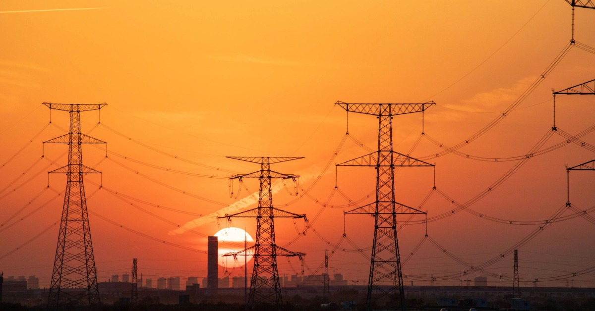 Electricity transmission towers and power lines during extreme heat at sunset, illustrating heat-related risks to energy and urban infrastructure.