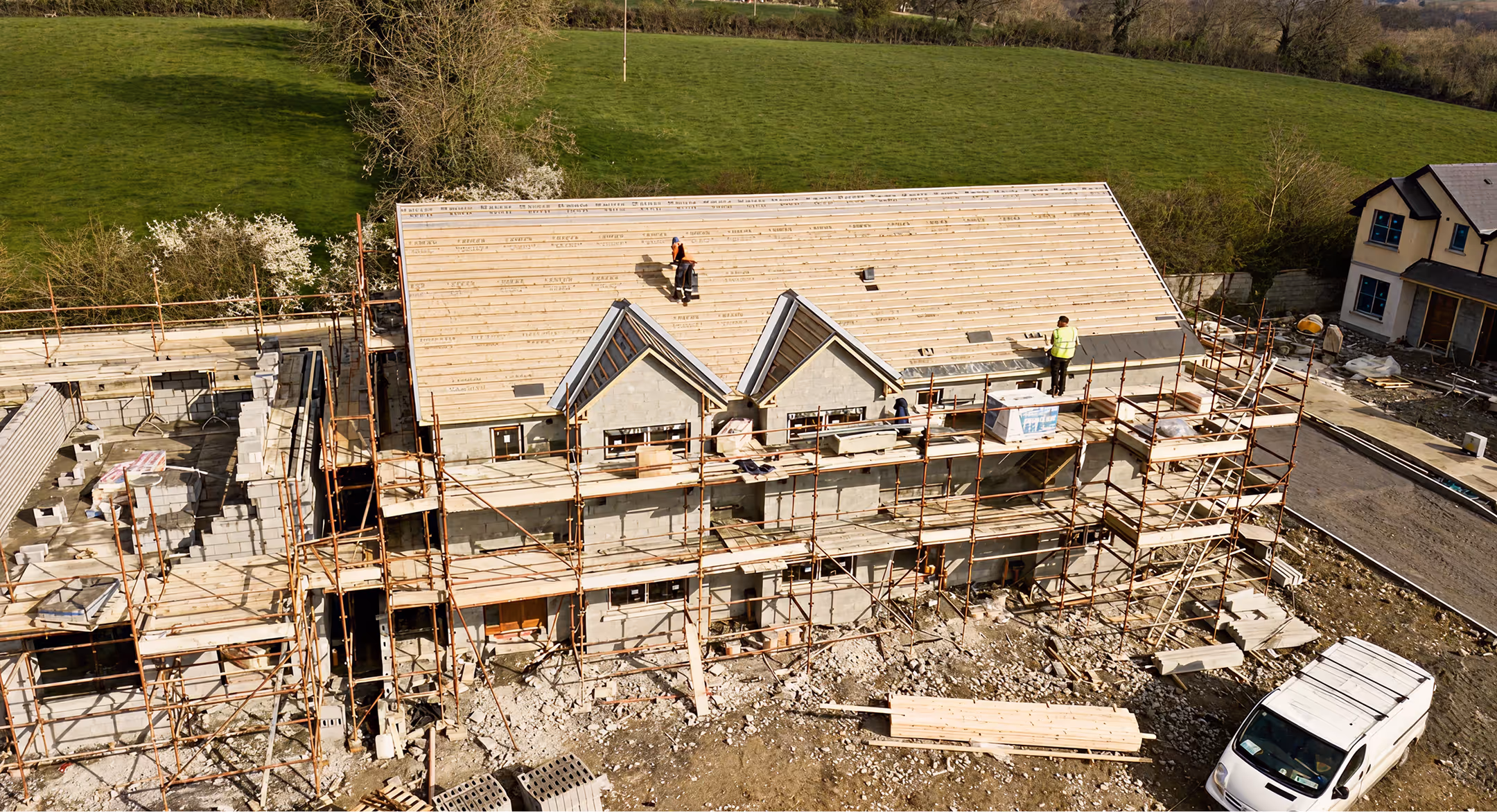 Construction site with a partially built house featuring scaffolding and workers installing roofing materials.
