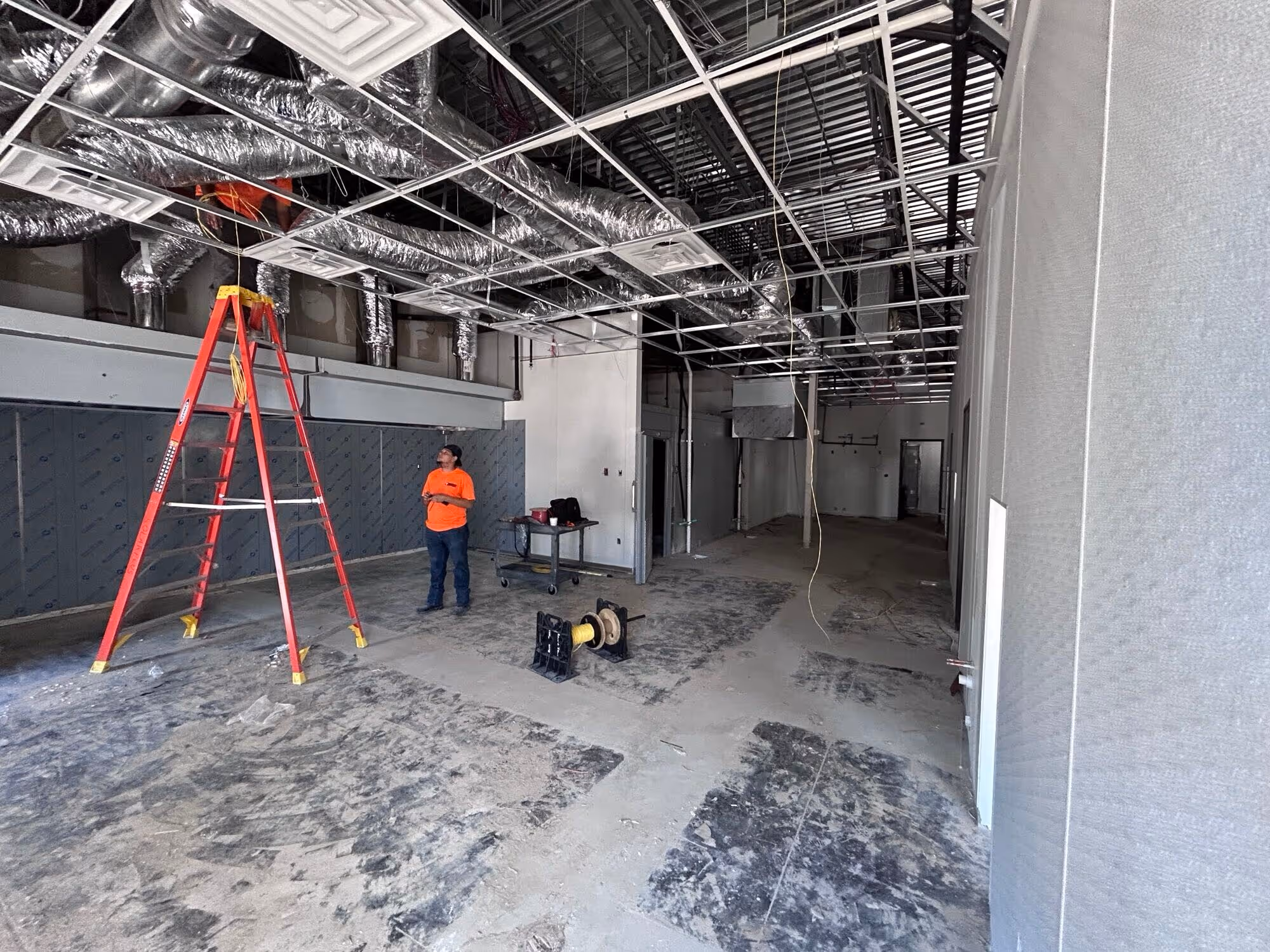 Large industrial warehouse interior with a concrete floor, metal staircase, black pickup truck, scissor lift, and overhead ductwork under construction. By Skyward
