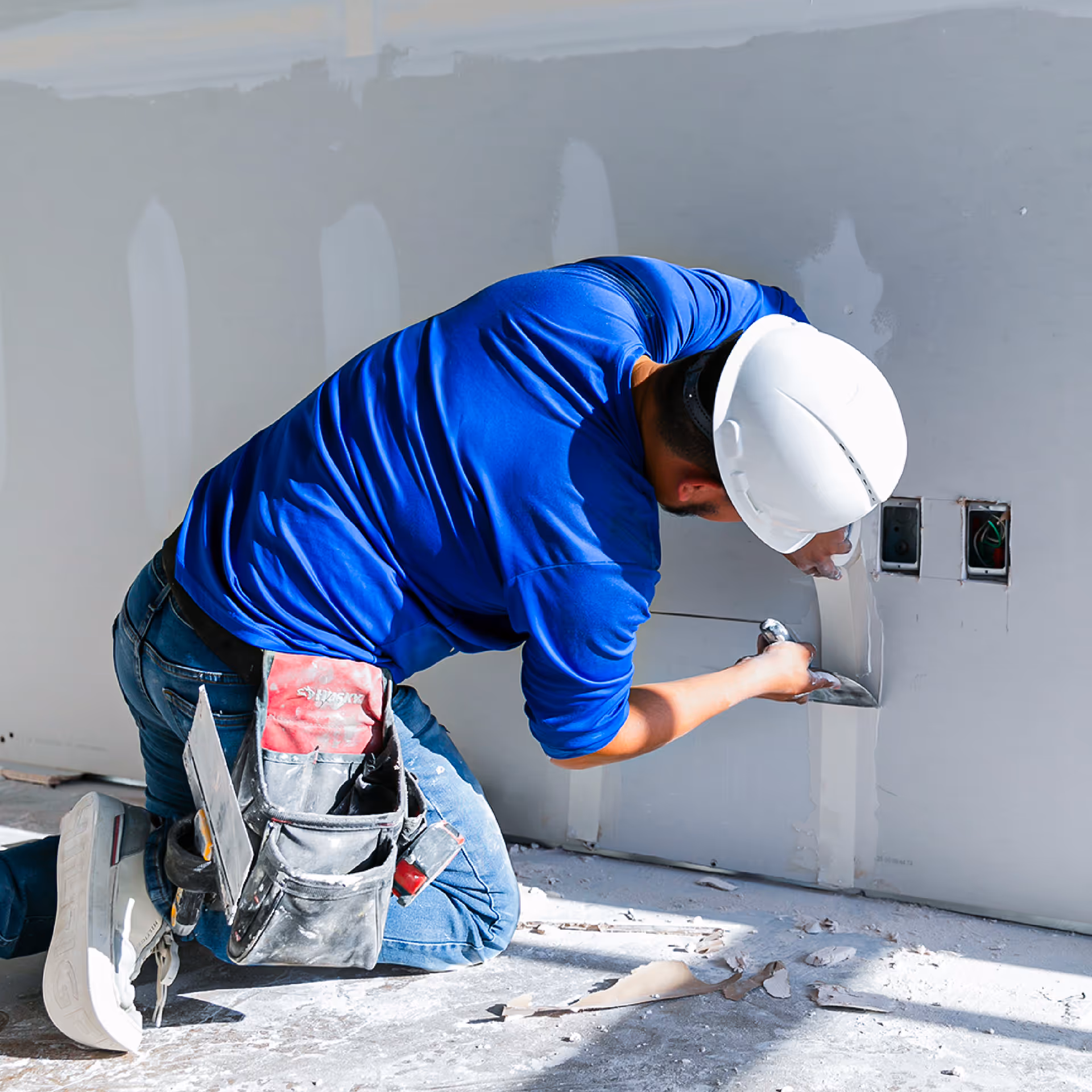 Bright, minimalistic room under renovation with tools in an open black case on the floor, large windows with greenery outside, and a modern wood stove on the right.