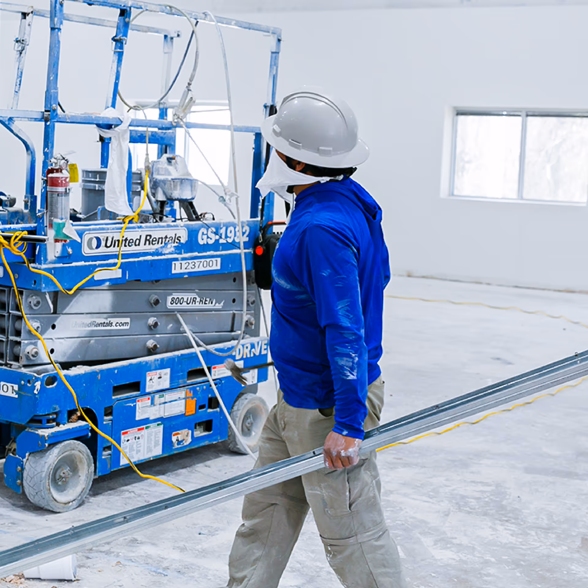 Construction worker wearing a white hard hat using a surveying instrument on a tripod.