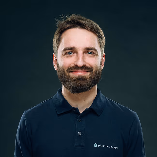 Smiling man with beard and short hair wearing a dark polo shirt with physioconcept logo on a dark background.