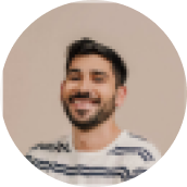 Smiling man with short dark hair and beard wearing a striped shirt on a beige background.