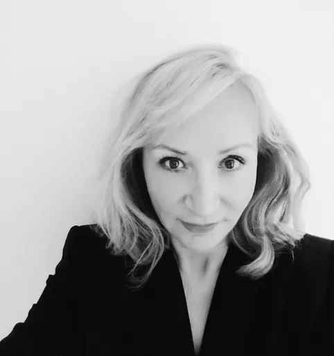 Black-and-white portrait of a woman with shoulder-length light hair wearing a dark blazer against a plain background.