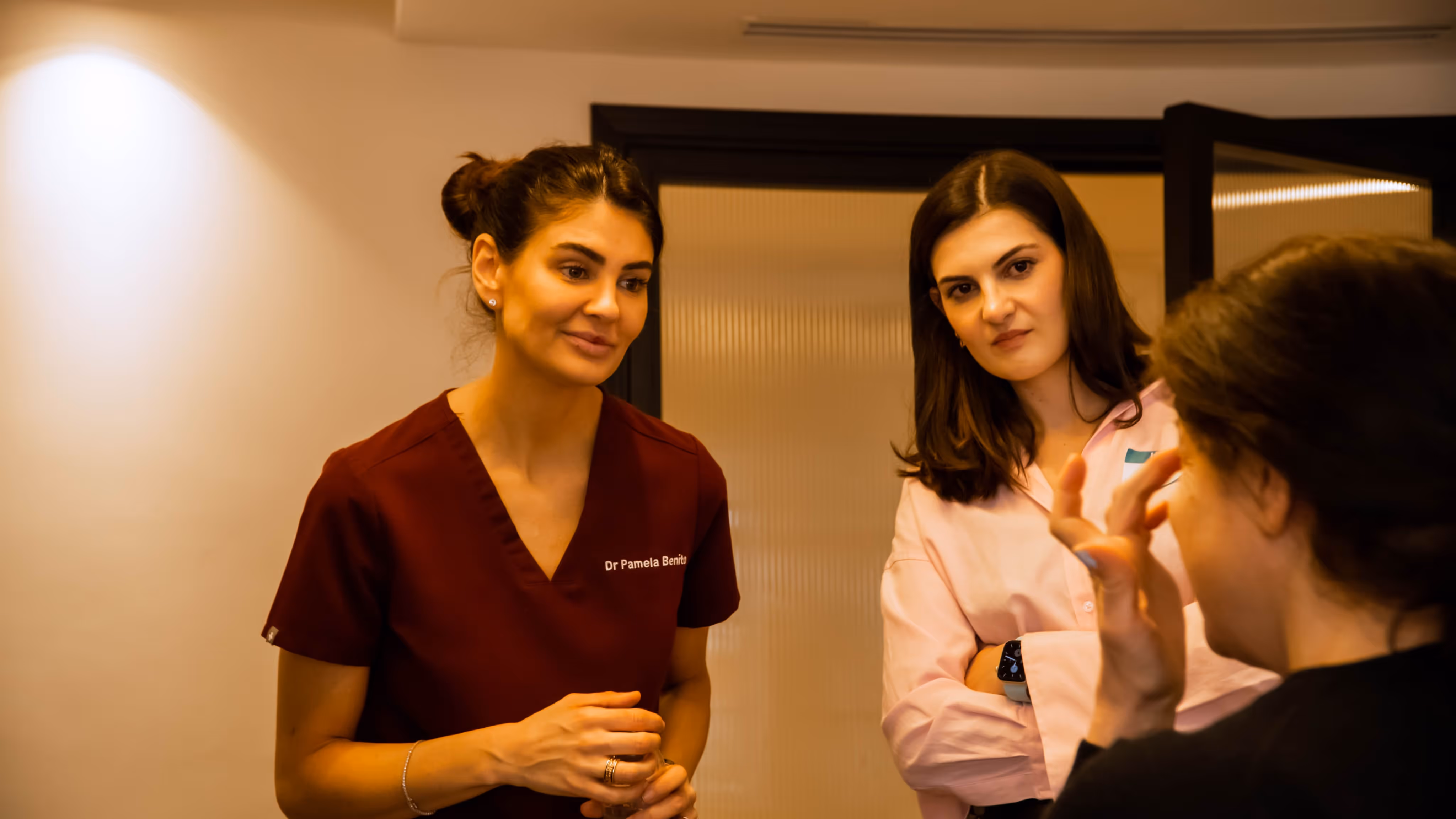 Two women attentively listening to a third woman who is speaking and gesturing with her hand.