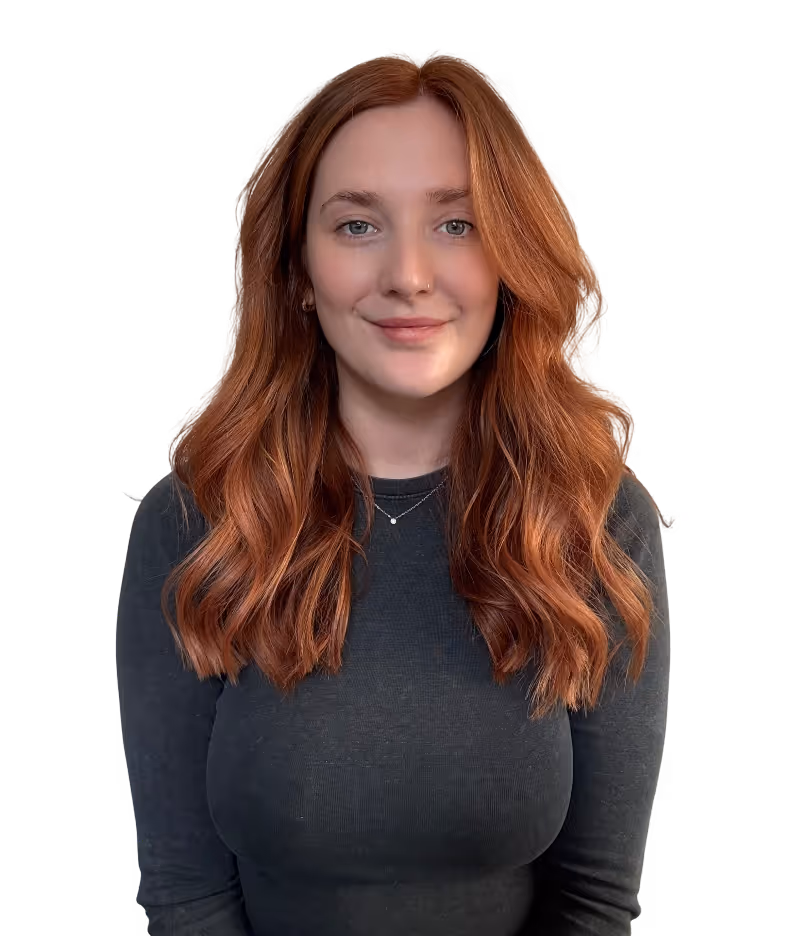 Smiling woman with long wavy red hair wearing a dark long-sleeve shirt and a delicate necklace.