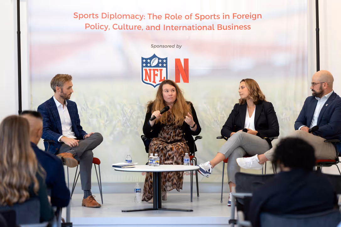 Panel discussion with four people seated on chairs in front of an audience, under a banner reading 'Sports Diplomacy: The Role of Sports in Foreign Policy, Culture, and International Business' sponsored by NFL and Netflix.