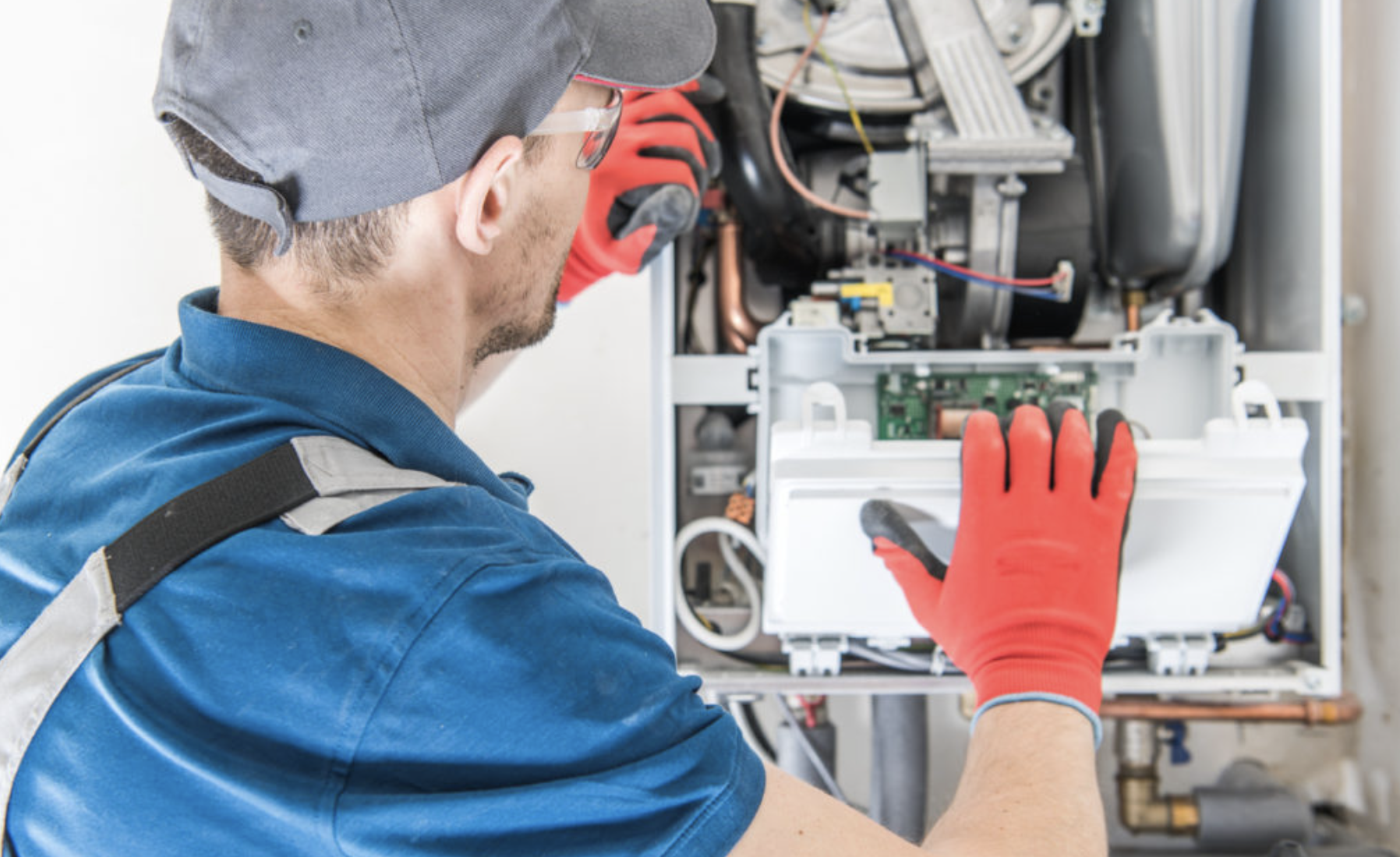Technician in blue shirt and red gloves working on an open heating system unit.