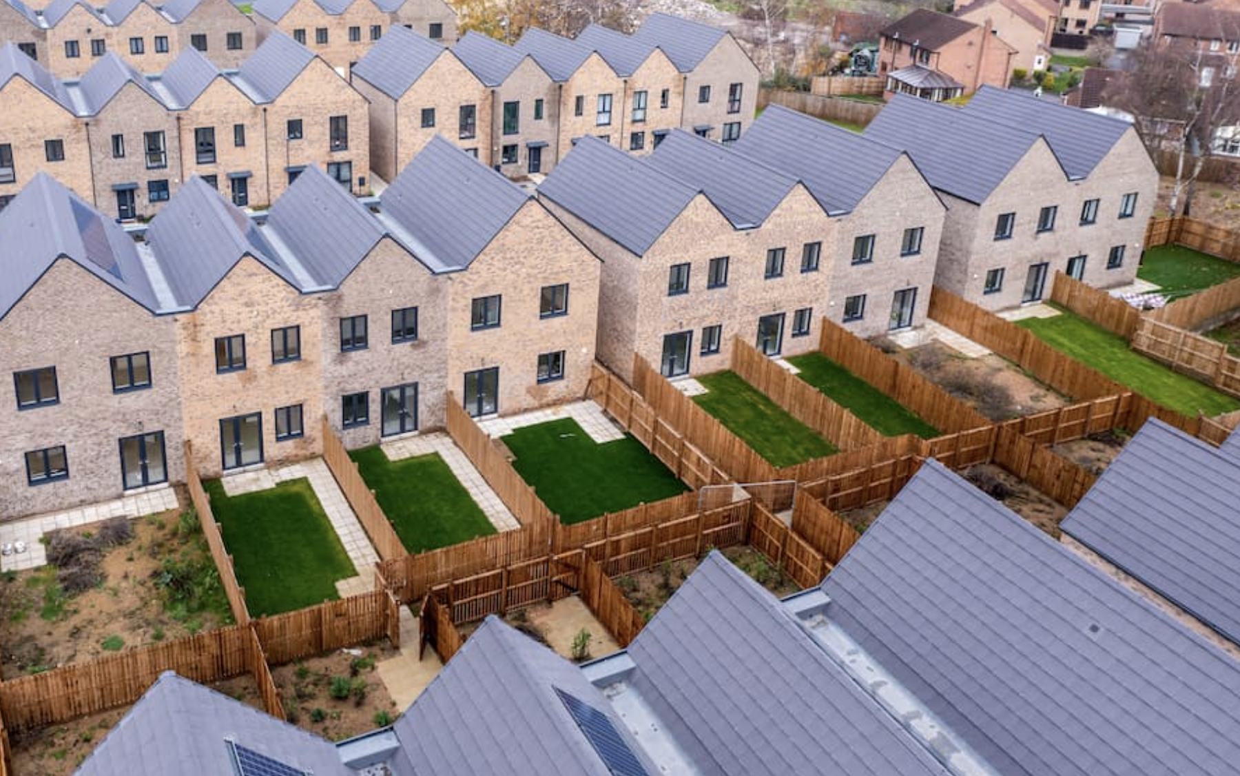 Aerial view of newly constructed modern brick townhouses with fenced backyards and green lawns.