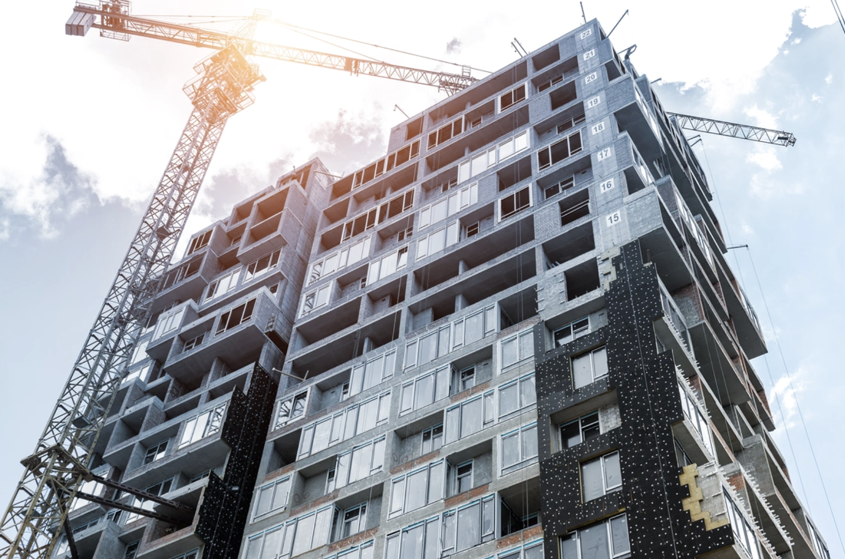 Under-construction high-rise building with cranes against a partly cloudy sky.