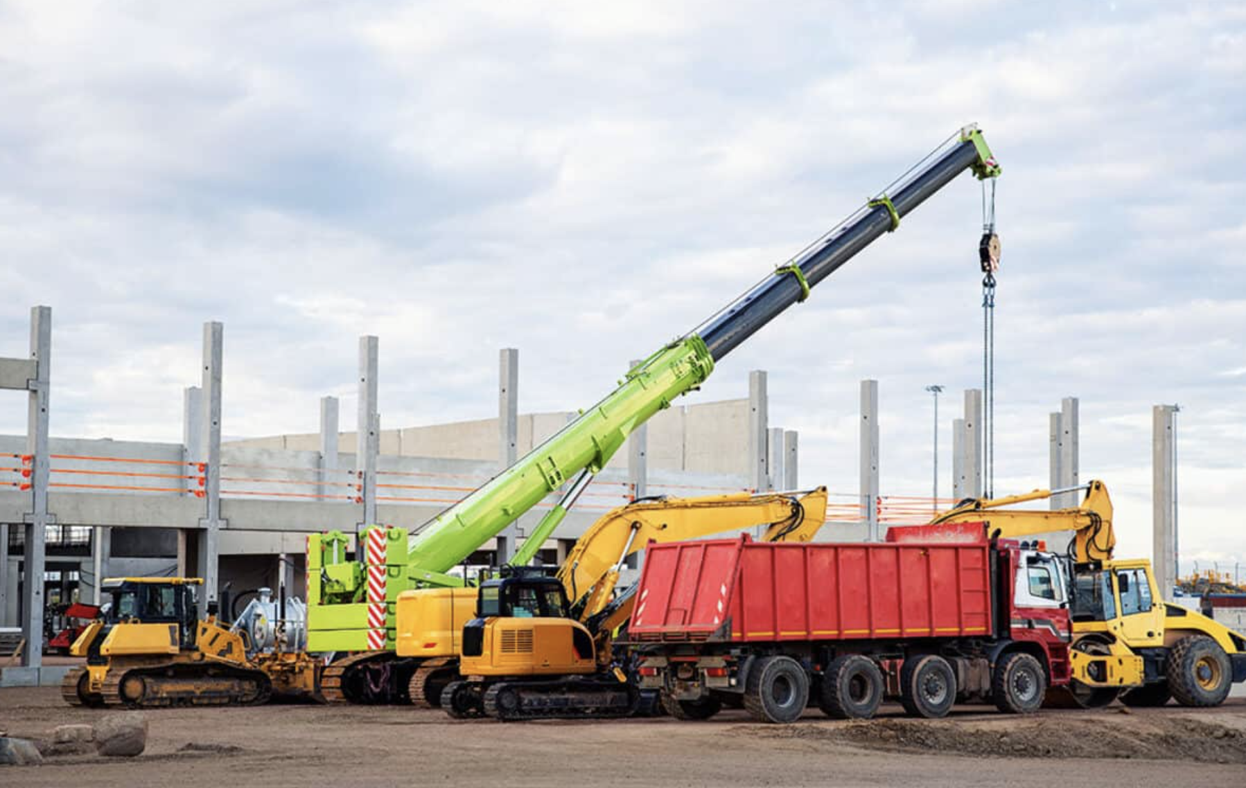 Construction site with a green crane, yellow excavators, and a red dump truck in front of a partially built concrete structure.