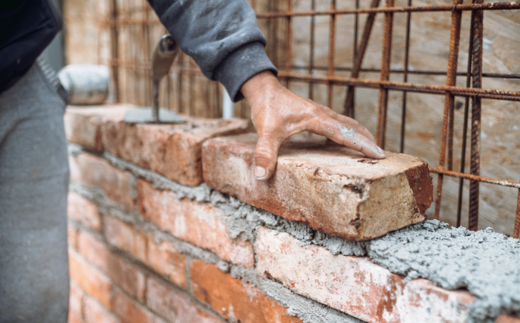 Close-up of a construction worker's hand laying a brick on a wall with wet mortar.