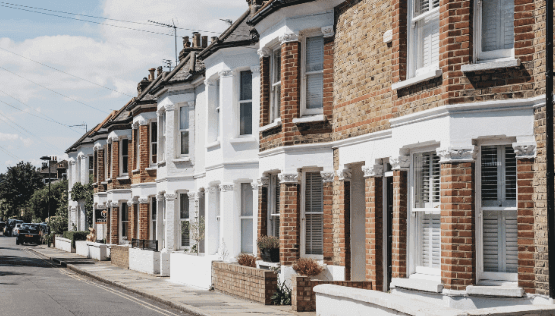 Row of traditional brick and white terraced houses on a sunny residential street.
