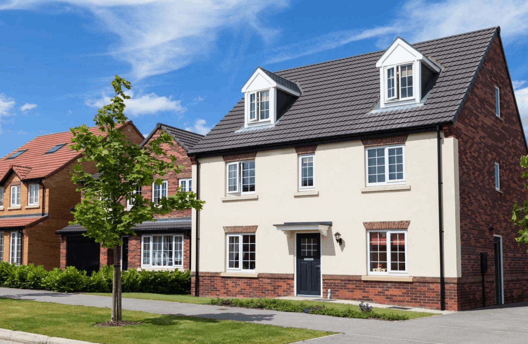 Modern two-story suburban house with cream and brick exterior, black front door, and dormer windows under a blue sky.