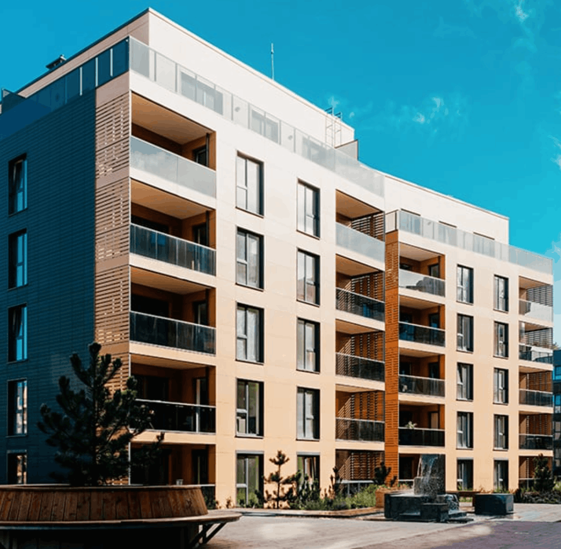 Modern five-story apartment building with balconies and glass railings under a clear blue sky.