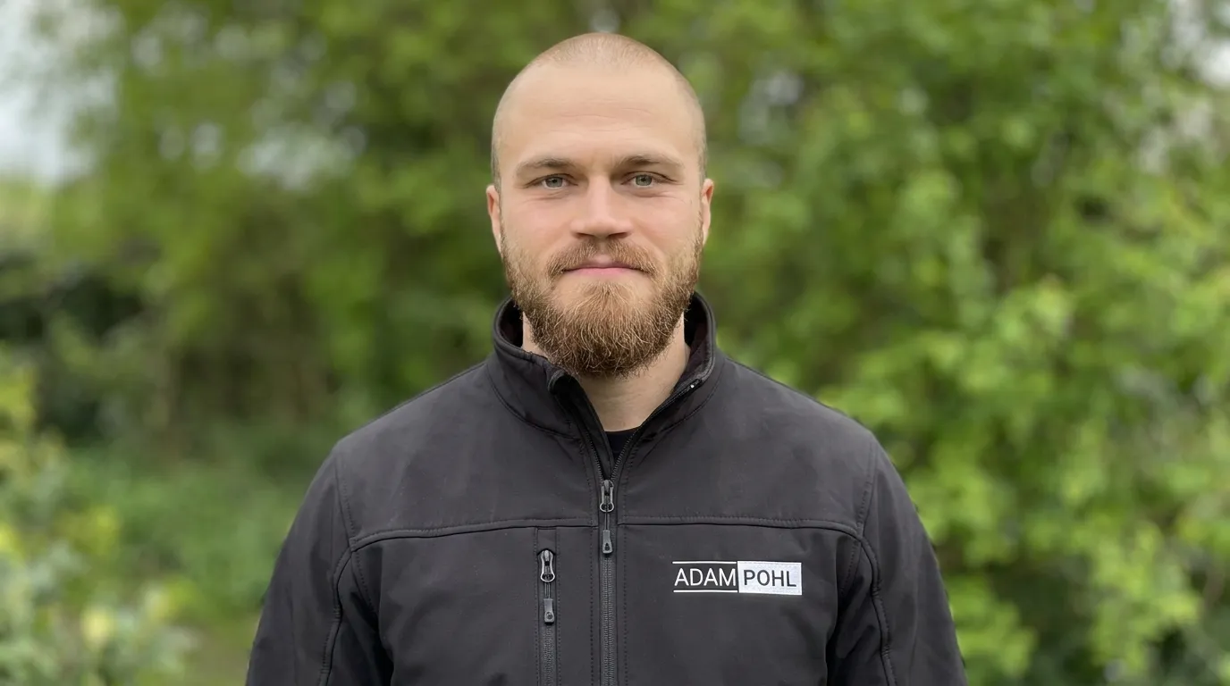 Adam Pohl in Arbeitsjacke mit Firmenlogo vor grünem Hintergrund