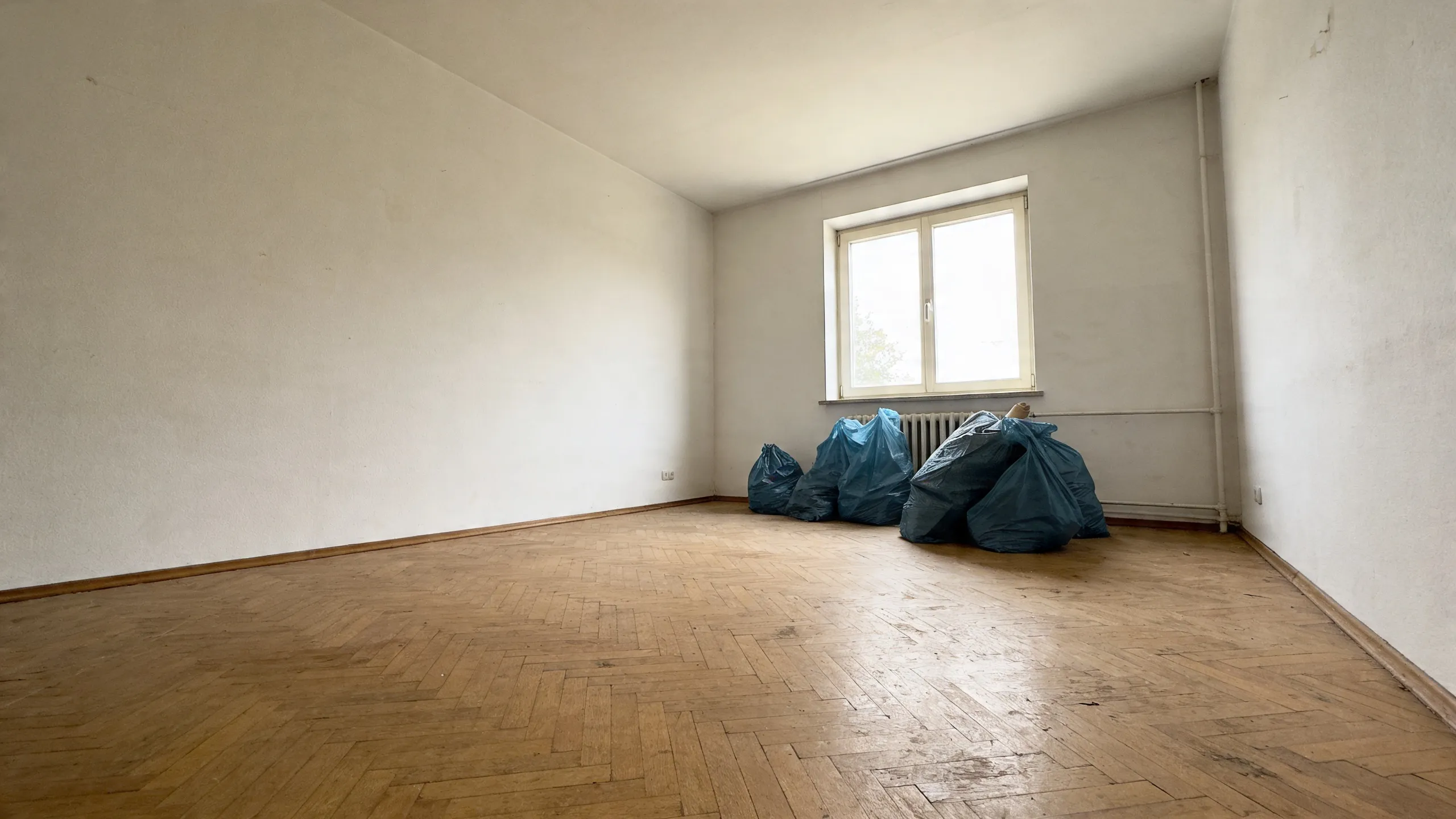 Geräumtes Zimmer mit Parkettboden, verschlossene Entsorgungssäcke stehen unter dem Fenster