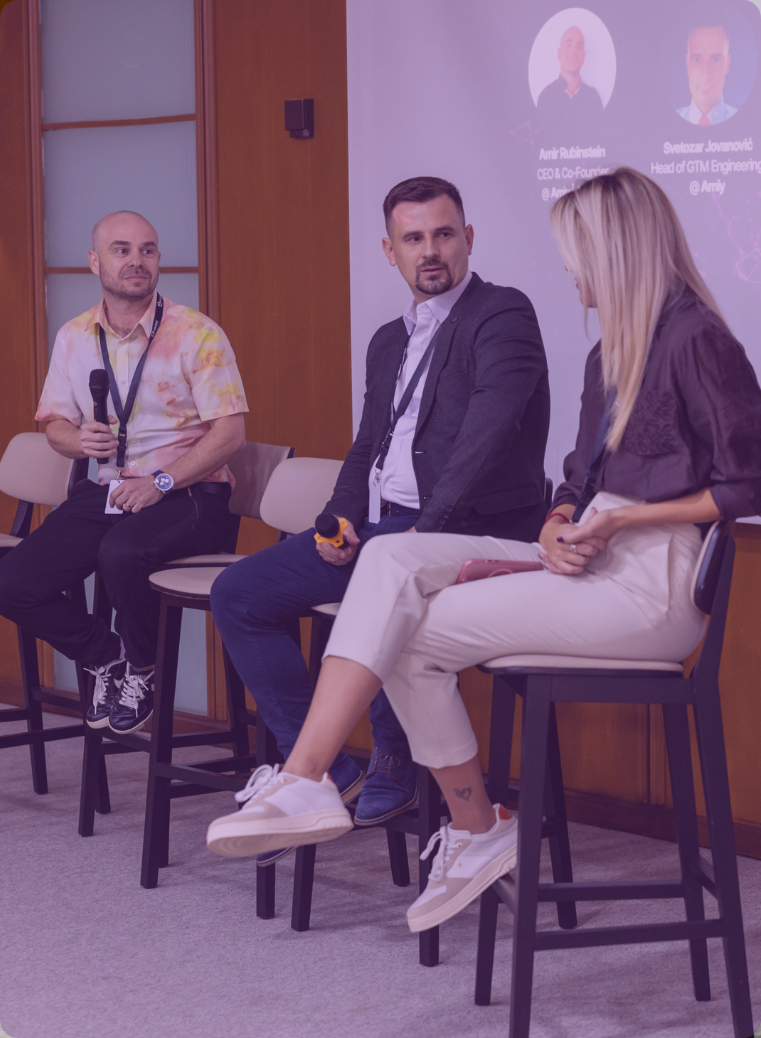 Three people seated on high stools holding microphones, participating in a panel discussion in a conference room.